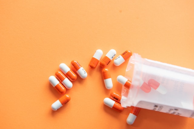A container of orange-white medical capsules spilled onto a tan surface.