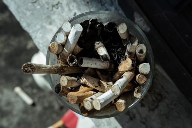 A glass filled to the brim with old cigarette butts.